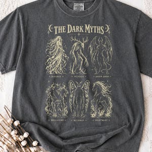May include: A charcoal grey t-shirt featuring a cream-coloured graphic titled THE DARK MYTHS. The print displays six mythical creatures labelled Banshee, Wendigo, Shadow Demon, Hellhound, Mothman, and Nightmare, arranged in two rows of three.