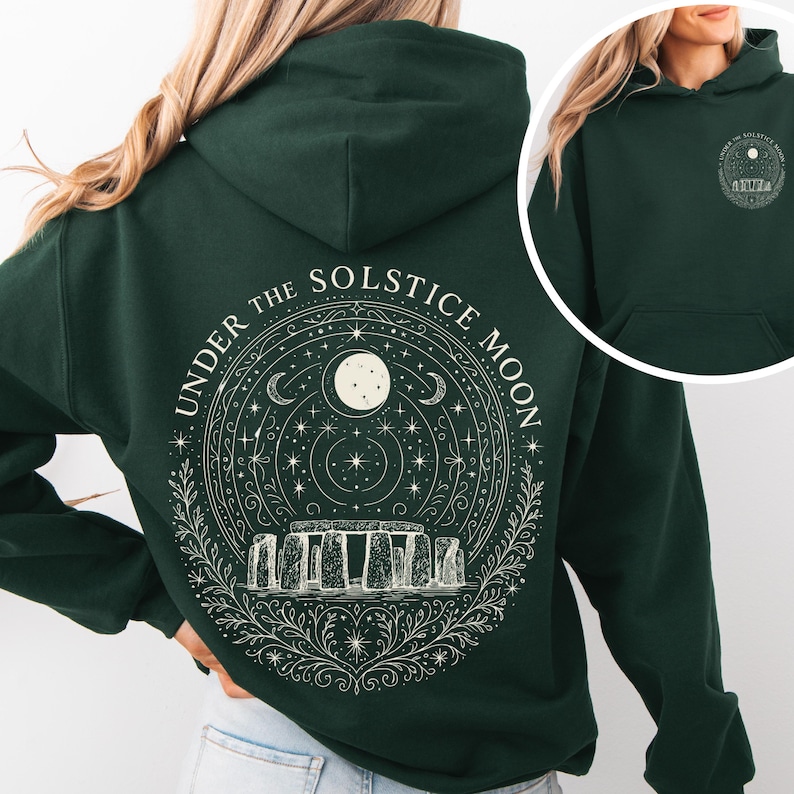 May include: Dark green hoodie with a white graphic on the back featuring Stonehenge, a full moon, stars, and the text "UNDER THE SOLSTICE MOON." A smaller version of the design is on the front.