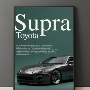 May include: A framed poster featuring a gray Toyota Supra sports car. The word "Supra" is displayed in large, white, stylized font above the Toyota logo. The poster has a dark green background and includes text describing the car's features.