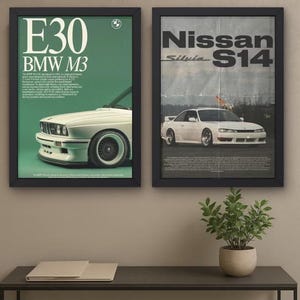Puede incluir: Dos láminas enmarcadas de arte automotriz. Una presenta un BMW M3 blanco con el texto "E30 BMW M3" en blanco y verde. La otra lámina muestra un Nissan Silvia S14 blanco con el texto "Nissan S14". Ambas láminas están enmarcadas en negro.
