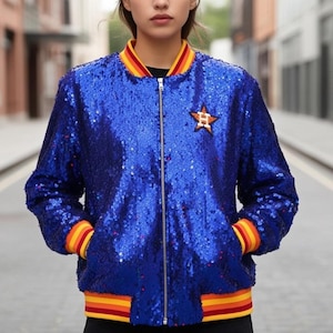 Könnte beinhalten: Eine leuchtend blaue Pailletten-Bomberjacke mit goldenem Reißverschluss und einem Sternaufnäher. Die Jacke hat gestreifte Bündchen und Kragen in Gelb, Orange und Rot. Ein stilvolles und auffälliges Oberbekleidungsstück.