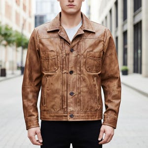 Puede incluir: Chaqueta de cuero marrón con cuello, dos bolsillos en el pecho y cierre de botones. La chaqueta tiene un aspecto desgastado y texturizado y se lleva sobre una camiseta gris. La chaqueta es de estilo clásico.