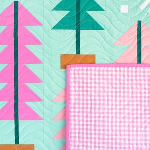 May include: A quilted fabric featuring a light mint green background with stylized trees in shades of pink, dark green, and brown. A section of the quilt is folded over to reveal a pink and white gingham pattern with a solid pink fabric border.