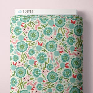 May include: A roll of fabric with a repeating floral pattern. The design features large teal flowers, small pink flowers, green leaves, and pink caterpillars on a cream background. The text "CLOUD9" is visible on the top.
