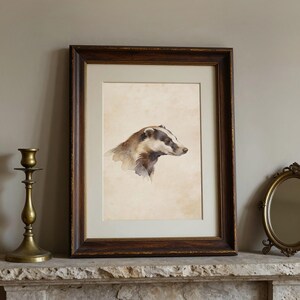 May include: A framed watercolour painting of a badger. The artwork features a badger in profile, with a black and white striped head and brown fur. The frame is dark wood. The painting is displayed on a stone mantelpiece, with a brass candlestick and a small mirror.