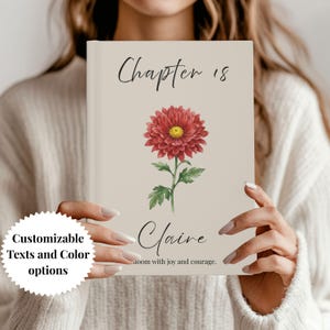 Pode incluir: Um livro personalizado com um design floral. A capa apresenta um crisântemo vermelho com centro amarelo, caule e folhas verdes, e o texto "Chapter 18" e "Claire". O livro também tem o texto "bloom with joy and courage."