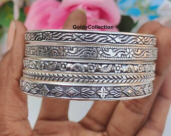 May include: A stack of silver bangles with intricate floral and geometric patterns. The bangles are held in a hand, with the brand name "GoldyCollection" visible. The bangles have detailed designs, including leaves, flowers, and other decorative elements.