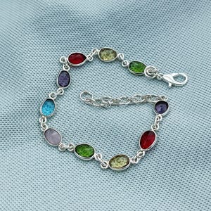 May include: A silver bracelet featuring oval-shaped gemstones in various colors, including red, green, blue, and purple. The bracelet has a delicate chain design and a secure clasp.