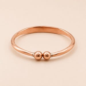 May include: A copper-colored bangle bracelet with two small, round, copper-colored beads at the center. The bracelet has a smooth, polished finish and a simple, elegant design. The bracelet is a piece of jewelry.
