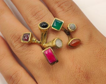 Könnte beinhalten: Ein einzigartiger goldfarbener Ring mit mehreren Edelsteinen in verschiedenen Formen und Farben, darunter Rot, Grün, Schwarz und Rosa. Das Design des Rings ist aufwendig, mit den Steinen auf filigranen Zweigen.