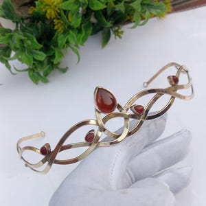 Peut inclure: Un diadème doré avec un design fluide et entrelacé. Il présente des pierres précieuses en forme de goutte et rondes, de couleur brun rougeâtre. Le design symétrique comporte des pierres précieuses espacées uniformément. Idéal pour les occasions spéciales.