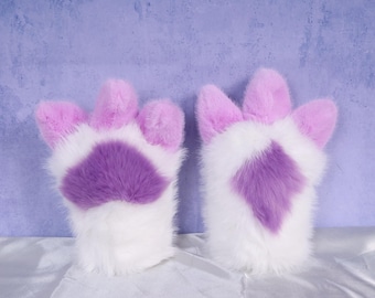 Puede incluir: Un par de guantes de pata de felpa y peludos. Los guantes son blancos con almohadillas púrpuras y puntas de color lavanda. Los guantes están diseñados para parecerse a las patas de los animales.
