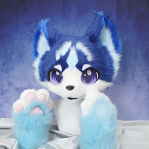 Puede incluir: Una cabeza de lobo de pelaje azul y blanco con grandes ojos morados y una nariz negra. La cabeza es parte de un disfraz, con patas de pelaje azul y blanco a juego con almohadillas rosas.