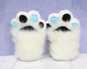 Puede incluir: Un par de guantes de pata de piel sintética blanca. Cada pata tiene almohadillas negras y azul claro. Los guantes están diseñados para parecerse a las patas de los animales, con una apariencia suave y esponjosa.