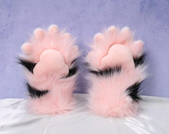 May include: A pair of pink and black faux fur paw gloves. The gloves have pink pads and claws, with black accents. The gloves are designed to resemble animal paws.
