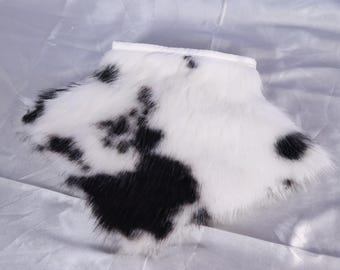 Op de afbeelding: Een wit en zwarte imitatiebont kraag met een koeienprint. De kraag is gemaakt van een zacht, pluizig materiaal en heeft een gebogen vorm. De zwarte vlekken zijn onregelmatig van vorm en verspreid over de witte achtergrond.