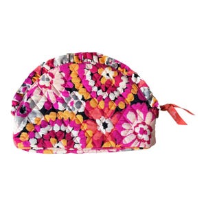 Puede incluir: Un neceser acolchado en forma de media luna con un vibrante estampado floral en tonos rosa, naranja, amarillo, blanco y negro. La bolsa tiene un tirador de cinta roja y un diseño acolchado.