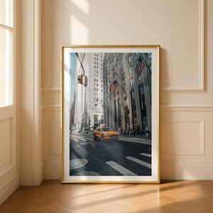 Könnte beinhalten: Gerahmtes Foto einer New Yorker Straßenszene. Ein gelbes Taxi fährt auf der Straße. Hohe Gebäude säumen die Straße, mit amerikanischen Flaggen, die aus den Fenstern hängen. Das Foto ist in einem goldenen Rahmen.