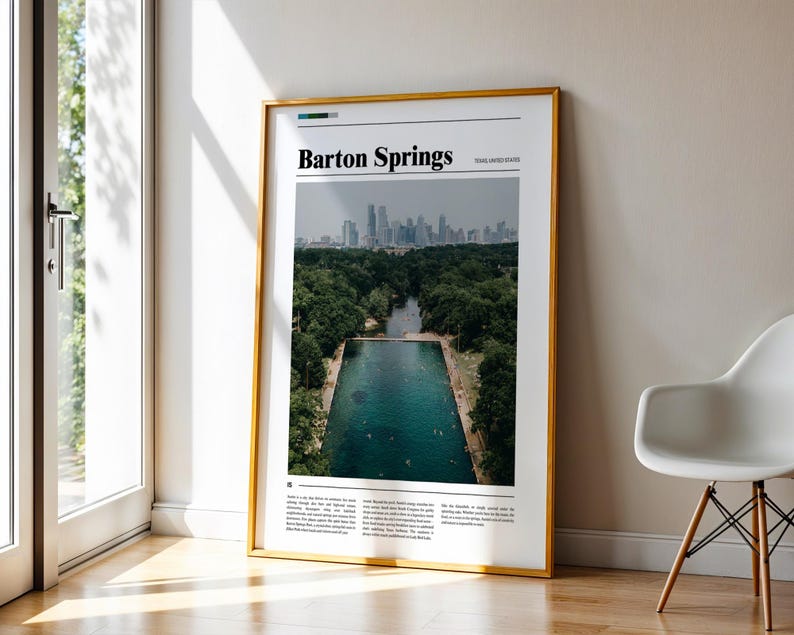 May include: A framed poster with a gold border, leaning against a wall. The poster features a photograph of Barton Springs in Austin, Texas, with the text "Barton Springs" at the top. The image shows a pool surrounded by trees and a city skyline in the background.