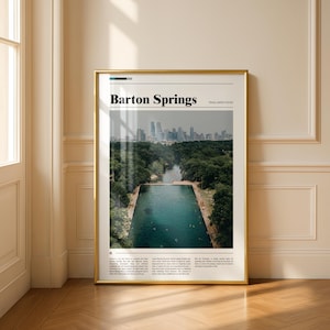 May include: A framed print featuring a photograph of Barton Springs in Austin, Texas. The image shows a rectangular pool of clear blue water surrounded by lush green trees, with a city skyline in the background. The words "Barton Springs" are printed at the top.