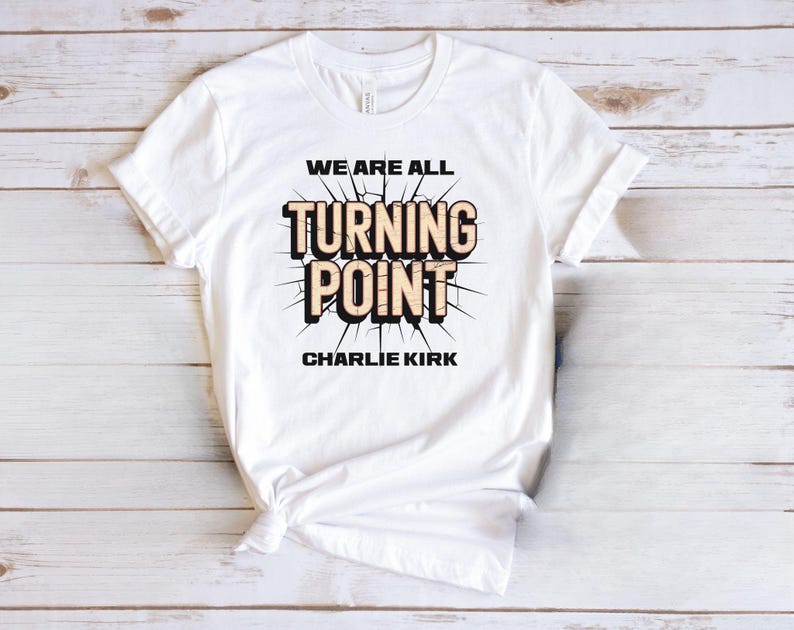 A white t-shirt with a graphic design featuring the text "WE ARE ALL TURNING POINT CHARLIE KIRK" printed on it.