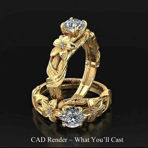 May include: Two gold rings with floral and leaf detailing. Each ring has a large, clear gemstone and smaller accent stones. The rings are set against a black background. Text at the bottom reads "CAD Render - What You'll Cast."