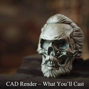 Könnte beinhalten: Eine detaillierte silberne Totenkopfskulptur mit stilisiertem Bart und Haaren. Der Schädel hat einen Schnurrbart und ist vor einem verschwommenen Hintergrund platziert. Der Text unten lautet "CAD Render - What You'll Cast."