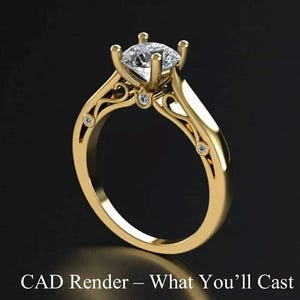 May include: A gold engagement ring with a large, clear, round-cut diamond center stone. The ring features a detailed filigree design on the band and smaller accent diamonds. Text at the bottom reads "CAD Render - What You'll Cast."