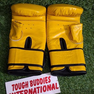 May include: A pair of yellow boxing gloves with black accents. The gloves are made of leather and have a padded design. The text "TOUGH BUDDIES INTERNATIONAL" is printed on a white card.