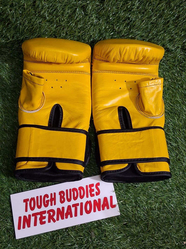 May include: A pair of yellow boxing gloves with black accents. The gloves are made of leather and have a padded design. The text "TOUGH BUDDIES INTERNATIONAL" is printed on a white card.