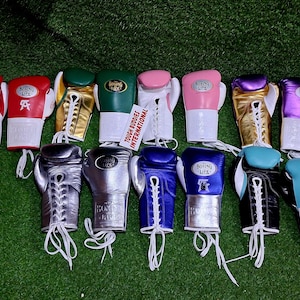 May include: A selection of multi-coloured boxing gloves, including red, pink, green, gold, silver, blue, black, and purple. Each glove has white laces and cuffs, with some displaying the text "Boxing Life" or "Tough Buddies International".