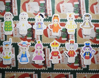 May include: A collection of colorful die-cut stickers featuring cartoon characters in various costumes. The stickers include characters dressed as a pear, a bear, a sailor, and a king, among others. The background is a festive Christmas-themed pattern.