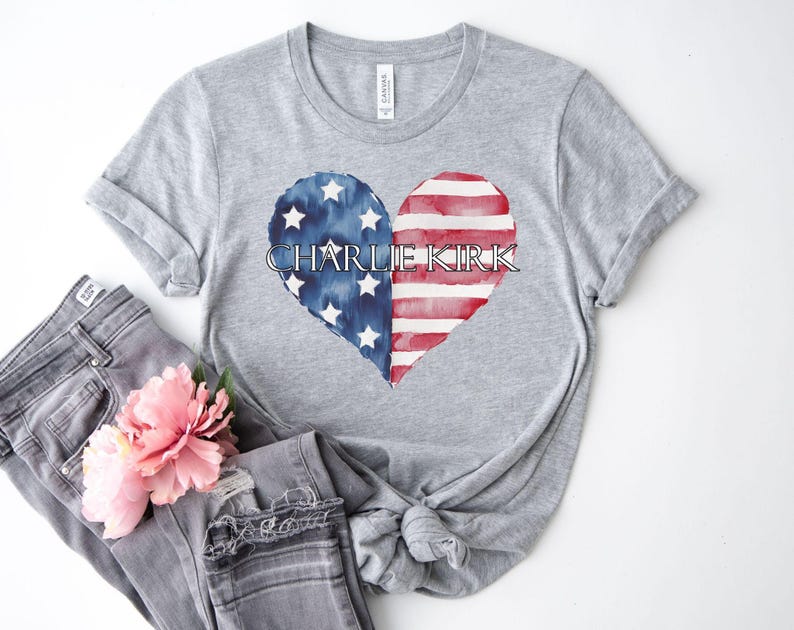 A gray t-shirt with a heart-shaped design featuring the text "CHARLIE KIRK" and an American flag pattern, along with a pink flower.