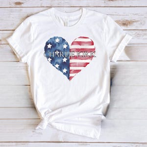 A white t-shirt with a heart-shaped design featuring the text "CHARLIE KIRK" and an American flag pattern.