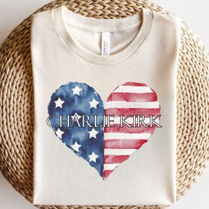 A white t-shirt with a graphic design featuring a heart shape in the colors of the American flag, with the name "Charlie Kirk" written on it.