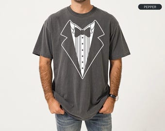 May include: A charcoal gray short-sleeve t-shirt featuring a white line art graphic of a tuxedo jacket, complete with a bow tie and a vertical striped shirt front. The top right corner of the image contains a small black label with the text PEPPER.