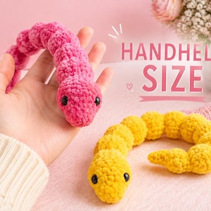 Puede incluir: Dos juguetes de ganchillo de felpa con forma de gusanos segmentados, uno de color rosa brillante y otro amarillo. Cada juguete presenta una cabeza redondeada con dos pequeños ojos de cuentas negras y una superficie de hilo suave y texturizada. El texto HANDHELD SIZE es visible.