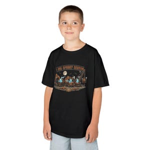 May include: A black short-sleeve t-shirt featuring a graphic print of construction vehicles operated by ghosts. The text reads A DIG SPOOKY SEASON. The design includes a full moon, bats, and pumpkins, set against a dark, textured ground.