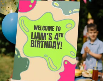May include: A party sign on an easel with the text "WELCOME TO LIAM'S 4TH BIRTHDAY!" in green and black. The sign has a beige background with pink and green abstract shapes. Balloons in blue, green, and gold are in the background.