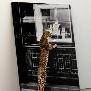 May include: A canvas print showing a leopard standing on its hind legs, looking into a jewellery shop window. The image is in black and white, with the leopard's spotted coat providing a contrast of colour and texture. The shop displays necklaces and other jewellery.