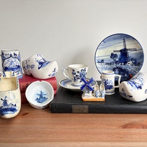 Può includere: Una collezione di oggetti in ceramica blu e bianca a tema olandese. Include zoccoli, una tazza, una tazza e un piattino, una piccola ciotola, un mulino a vento decorativo, un piatto e un piccolo boccale.