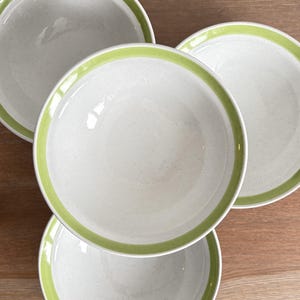 Puede incluir: Cuatro platos de cerámica blanca con un diseño moteado y un borde verde brillante. Los platos están dispuestos sobre una superficie de madera, mostrando su estética limpia y moderna. Ideal para servir comidas.