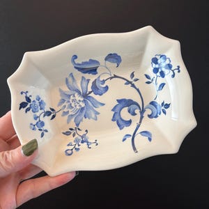 May include: A white ceramic dish with a scalloped edge, decorated with blue floral patterns. The rectangular dish features a central floral design and delicate blue accents, ideal for serving small items.