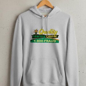 May include: A light gray hoodie with a front pocket and a drawstring hood. The front features a graphic with the words "Quality Learing Center" and "1-800-FRAUD" in yellow, green, and orange.