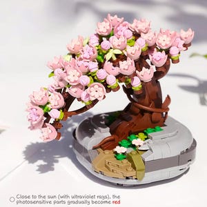 May include: A miniature cherry blossom tree model with pink flowers, brown trunk, and a gray base. The model includes the text: "Close to the sun (with ultraviolet rays), the photosensitive parts gradually become red."