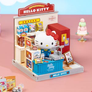 May include: A Hello Kitty supermarket playset featuring a white Hello Kitty figure with a red bow behind a blue checkout counter. The set includes shelves stocked with miniature snacks, a red refrigerator, a cash register, and signage reading Hello Kitty.