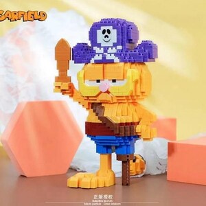 May include: A Garfield building block figure in a pirate costume, holding a wooden sword. The figure is primarily orange with blue shorts and a purple pirate hat. The Garfield logo is in the upper left corner.