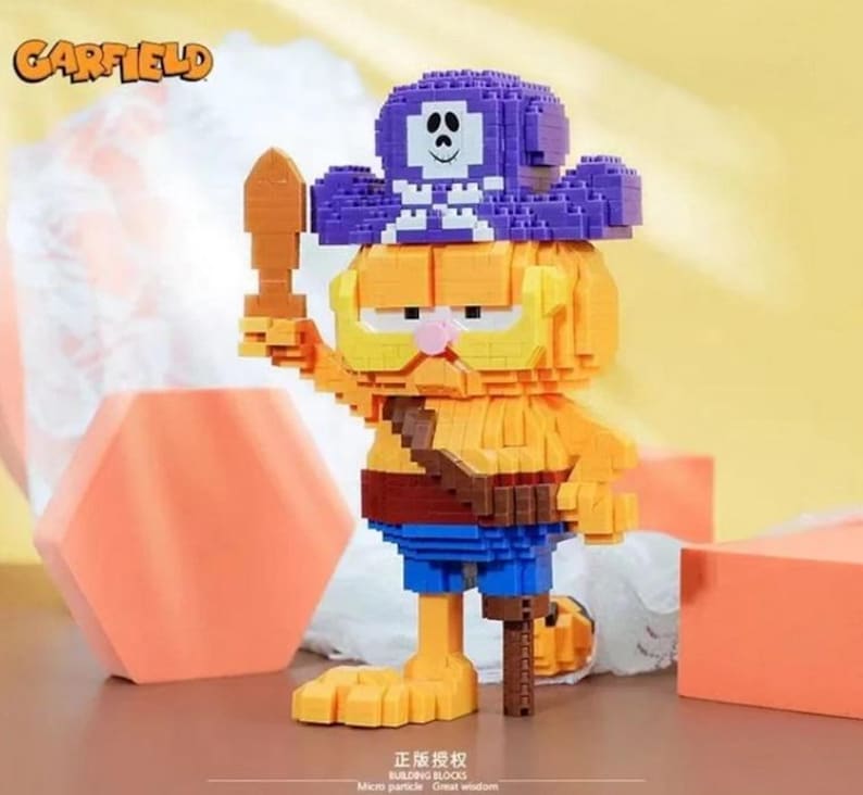 May include: A Garfield building block figure in a pirate costume, holding a wooden sword. The figure is primarily orange with blue shorts and a purple pirate hat. The Garfield logo is in the upper left corner.