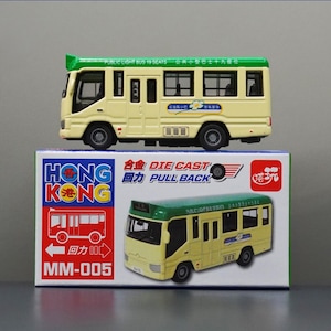 May include: A die-cast toy bus in yellow and green, with the text "PUBLIC LIGHT BUS 19 SEATS" on the roof. The bus sits atop a box with the words "HONG KONG" and "DIE CAST PULL BACK" printed on it. The box also features a red bus illustration.