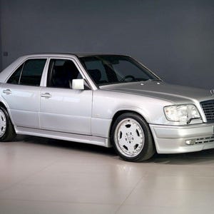 Op de afbeelding: Zilverkleurige sedan met een klassiek ontwerp. De auto heeft een slanke carrosserie, lichtmetalen velgen en een opvallende grille. Het voertuig staat in een goed verlichte ruimte, wat de strakke lijnen en de algehele esthetiek benadrukt.